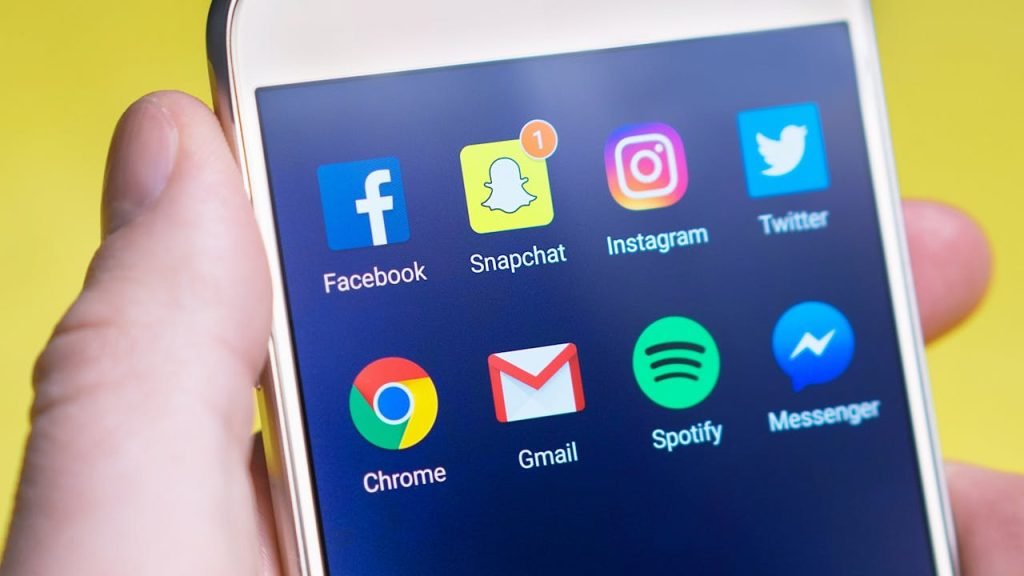 A persons hand holding a smartphone displaying social media and communication apps.
